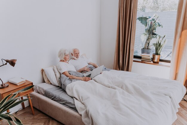 Lindo casal de idosos curtindo o tempo juntos em casa - casal de idosos moderados navegando na internet em um laptop