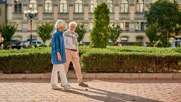 Lindo casal de idosos falando sobre algo enquanto caminhava no parque em um dia ensolarado