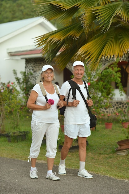 Lindo casal de idosos felizes descansando em um resort tropical com mochilas