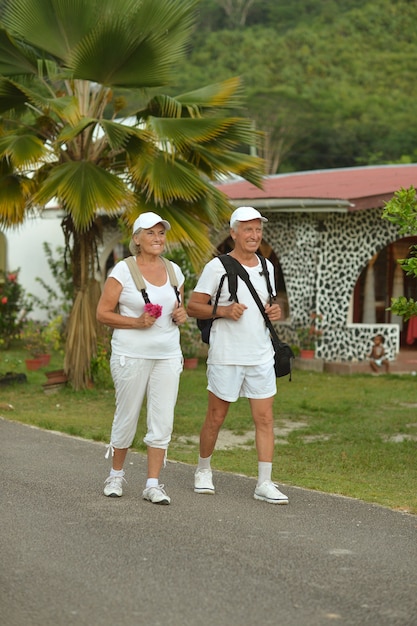Lindo casal de idosos felizes descansando em um resort tropical com mochilas