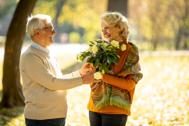 Lindo casal de idosos se abraçando com um buquê de flores no parque outono