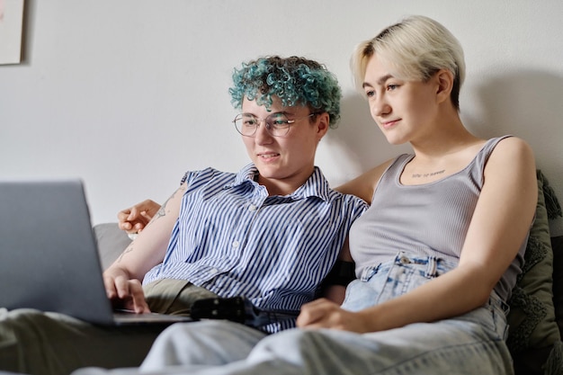 Lindo casal de lésbicas relaxando no quarto e assistindo filme no laptop