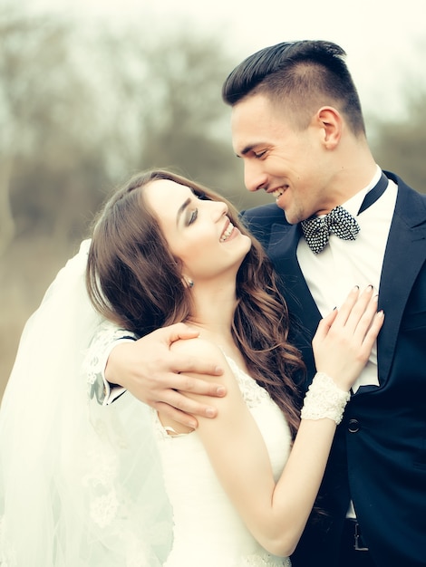 Lindo casal de noivos abraçando uma linda mulher feliz ao ar livre