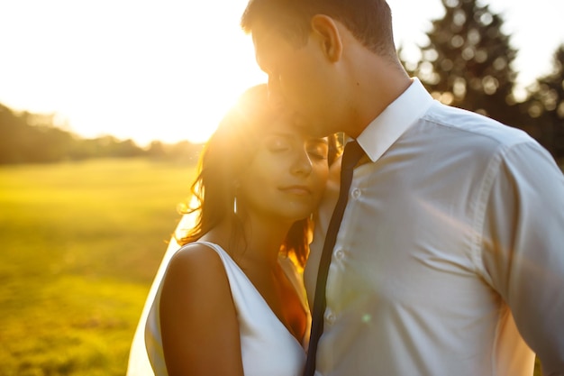 Lindo casal de noivos ao pôr do sol Noiva noivo em traje de casamento com buquê de flores Romântico