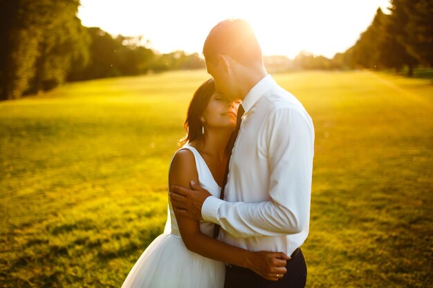 Foto lindo casal de noivos ao pôr do sol noiva noivo em traje de casamento com buquê de flores romântico