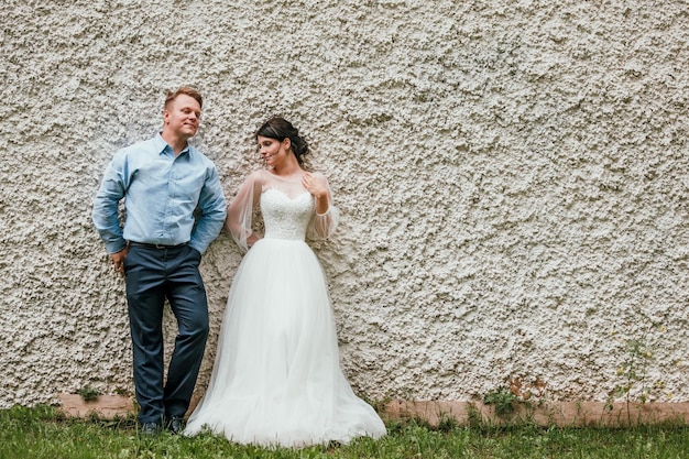 Lindo casal de noivos no estilo preto e branco em pé perto da parede