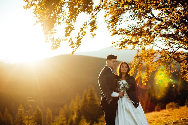 Lindo casal de noivos noivos apaixonados no fundo das montanhas o noivo em um lindo terno e a noiva em um vestido branco de luxo o casal de noivos está andando