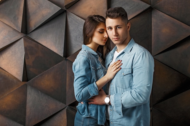 Lindo casal em roupas jeans da moda se abraçando perto de uma parede de madeira moderna