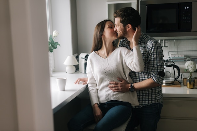 Lindo casal feliz se beijando na cozinha perto da janela