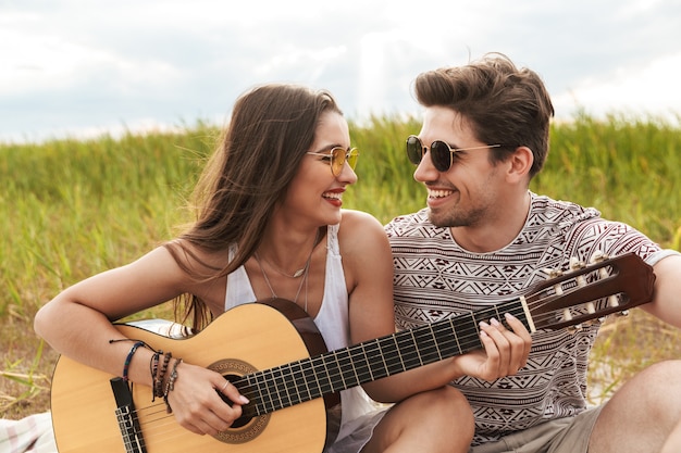 Lindo casal feliz sentado no parque, tocando violão, relaxando