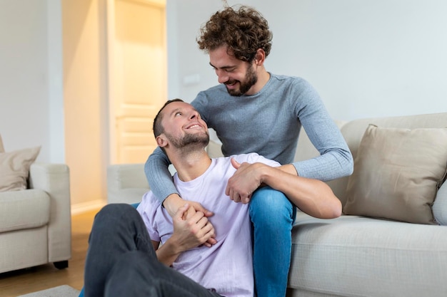 Lindo casal gay beijando enquanto está sentado em sua sala de estar em casa dois românticos jovens amantes do sexo masculino se divertindo dentro de casa jovem casal gay morando juntos