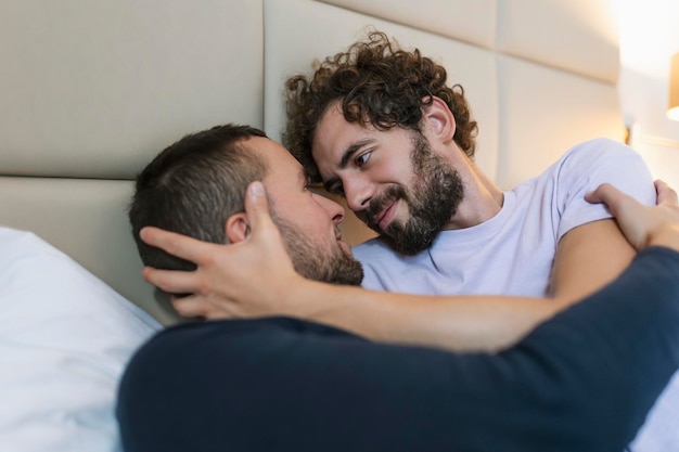 Lindo casal gay deitado na cama juntos Romântico jovem casal gay se abraçando carinhosamente em seu quarto Dois jovens amantes masculinos alegres se unindo carinhosamente em casa