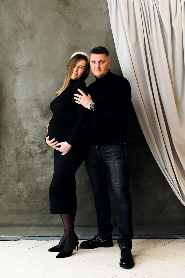Foto lindo casal grávida vestida com lindas roupas pretas abraços. mulher grávida com um vestido abraça o marido em casa. uma família grávida se alegra com a reposição futura