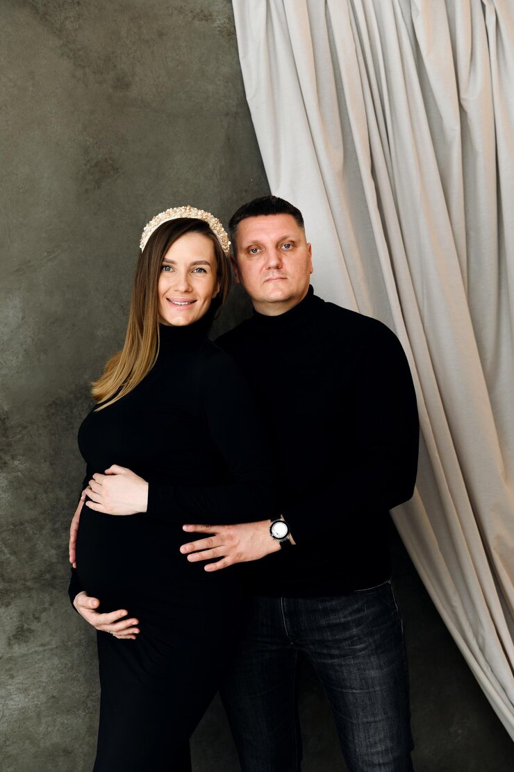 Foto lindo casal grávida vestida com lindas roupas pretas abraços. mulher grávida com um vestido abraça o marido em casa. uma família grávida se alegra com a reposição futura