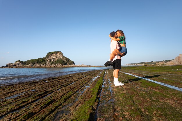 Lindo casal heterossexual em uma praia rochosa se abraçando e beijando no país basco.