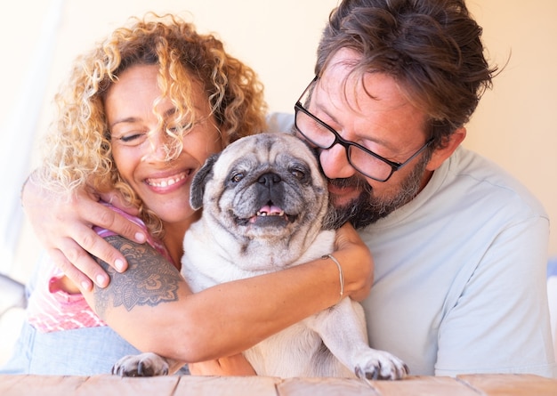 Foto lindo casal, homem e mulher, apaixonados por seu cachorro pug claro, amigos eternos