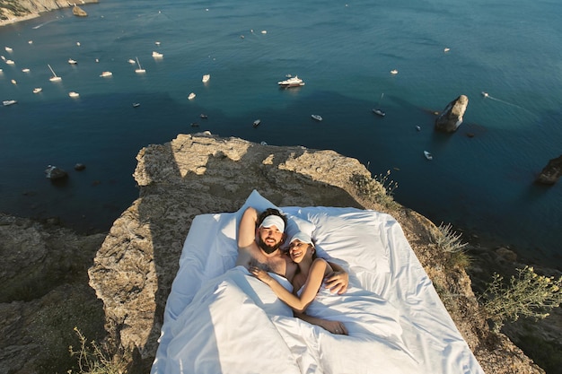 Lindo casal jovem acorda de manhã em uma cama branca em um penhasco com vista para o mar