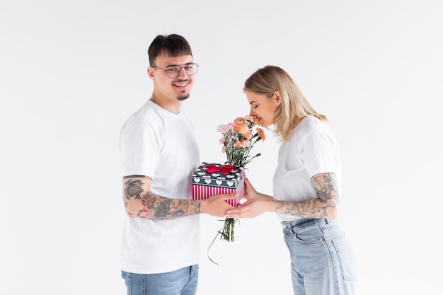 Lindo casal jovem apaixonado em casa comemorando com uma caixa de presente e flores