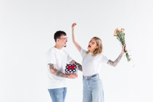 Lindo casal jovem apaixonado em casa comemorando com uma caixa de presente e flores