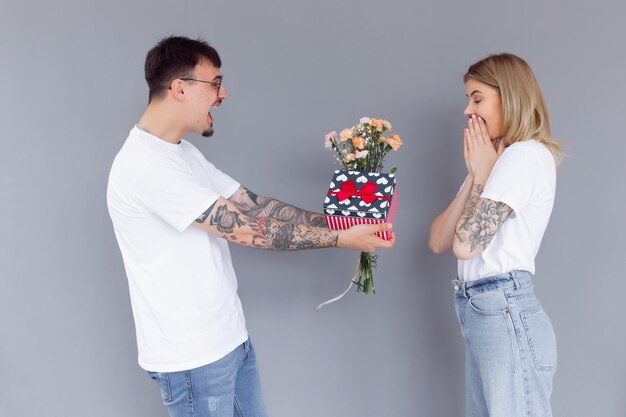 Lindo casal jovem apaixonado em casa comemorando com uma caixa de presente e flores