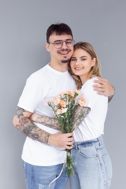 Lindo casal jovem apaixonado em casa comemorando com uma caixa de presente e flores
