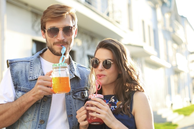 Lindo casal jovem caminhando pela rua da cidade, sorrindo e bebendo coquetéis frescos.