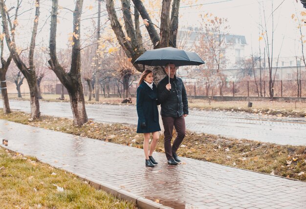 Lindo casal jovem caminhando sob um guarda-chuva no beco de outono