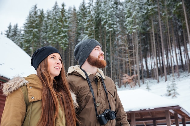 Lindo casal jovem com câmera fotográfica em pé curtindo a floresta de inverno