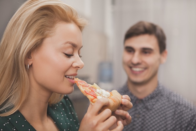 Lindo casal jovem comendo pizza juntos na cozinha