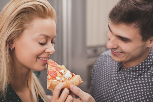 Lindo casal jovem comendo pizza juntos na cozinha