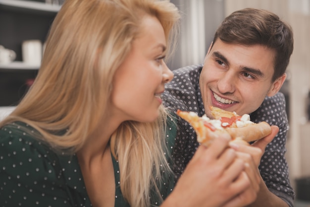 Foto lindo casal jovem comendo pizza juntos na cozinha