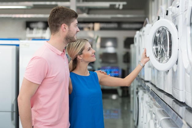 Lindo casal jovem comprando máquina de lavar roupa no departamento de produtos de uma mercearia supermercado raso de campo