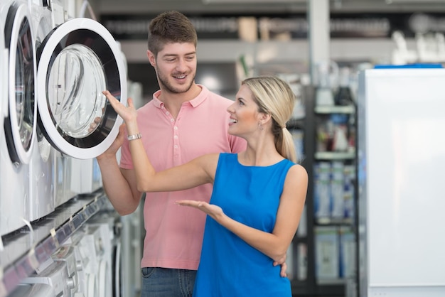 Lindo casal jovem comprando máquina de lavar roupa no departamento de produtos de uma mercearia supermercado raso de campo
