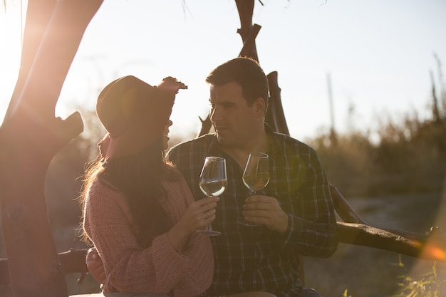 Lindo casal jovem conversando e desfrutando de uma taça de vinho em um vinhedo com a luz do sol por trás.