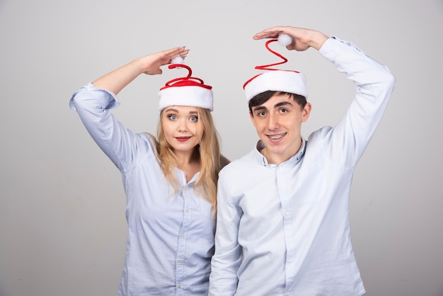 Lindo casal jovem dançando com gorros na parede cinza.