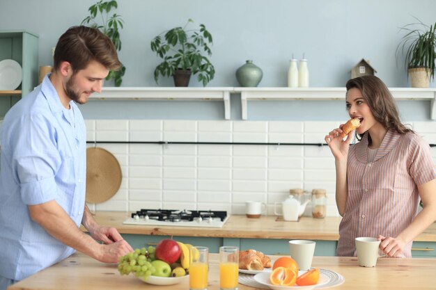 Lindo casal jovem de pijama está olhando um para o outro e sorrindo enquanto cozinha na cozinha em casa.