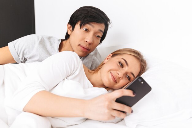 Lindo casal jovem, deitado na cama, jovem usando telefone celular