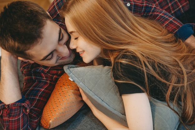 Lindo casal jovem encostado em uma cama se divertindo juntos, sorrindo em casa.