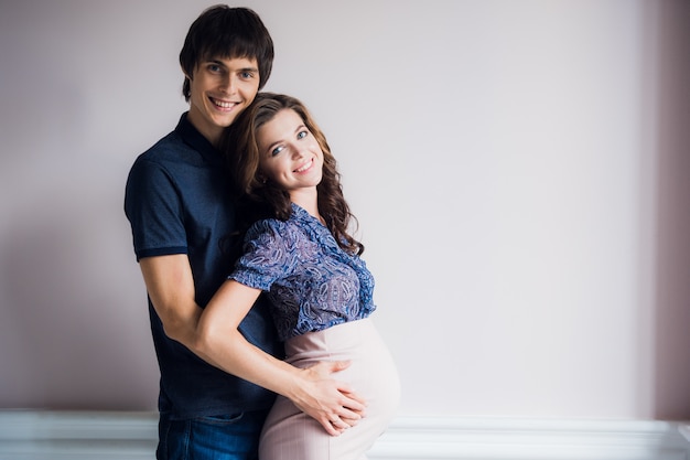 Foto lindo casal jovem esperando bebê ficar em frente a parede em casa.