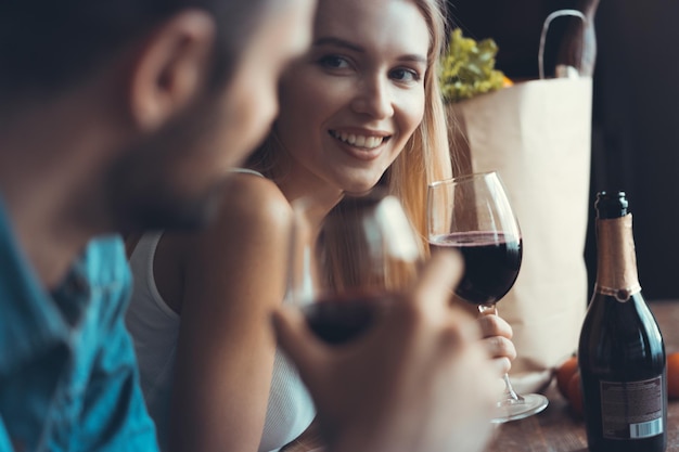 Lindo casal jovem está bebendo vinho e sorrindo enquanto cozinha na cozinha em casa