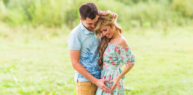 Lindo casal jovem está fazendo o coração de dedos e sorrindo na natureza.