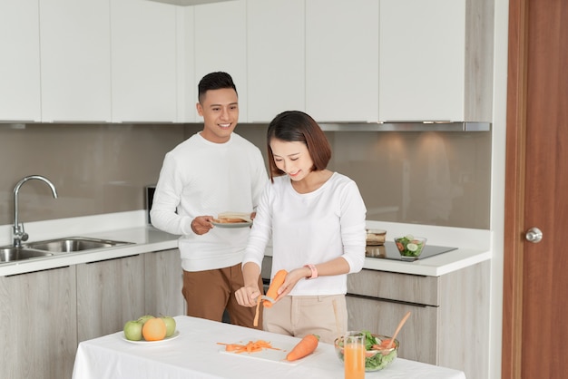 Lindo casal jovem está se alimentando e sorrindo enquanto cozinha na cozinha de casa