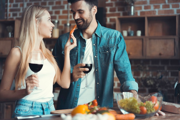 Lindo casal jovem está se alimentando e sorrindo enquanto cozinha na cozinha em casa.