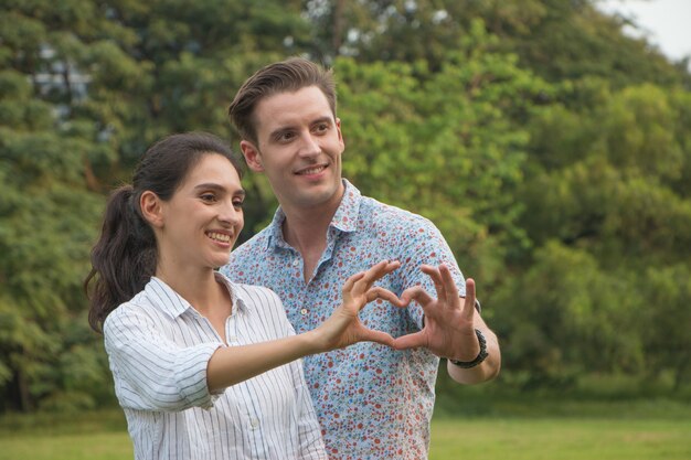 Lindo casal jovem feliz fazendo formato de coração com a mão ao ar livre