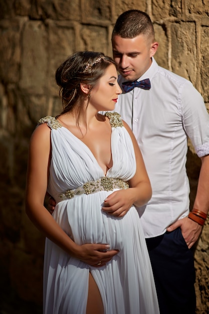 Lindo casal jovem, marido e mulher grávida em um vestido de renda branca nos braços um do outro
