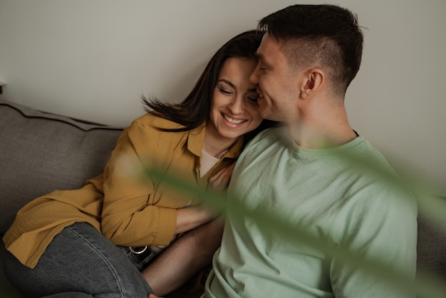 Lindo casal jovem mostrando sentimento romântico um para o outro, sentado no sofá da sala de estar. Família feliz se mudando para um novo apartamento.