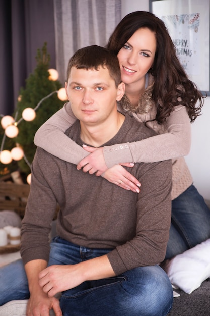 Lindo casal jovem relaxando em uma sala de estar com árvore de ano novo