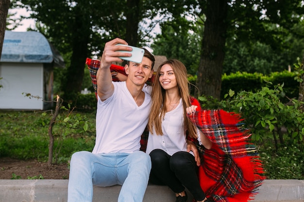 Lindo casal jovem relaxando no parque e fazendo selfie