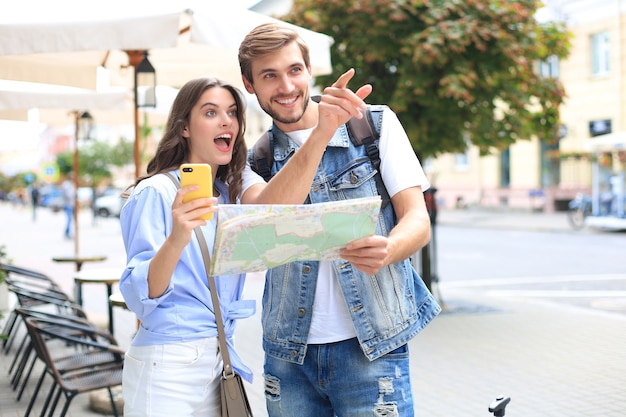 Lindo casal jovem segurando um mapa e sorrindo em pé ao ar livre.