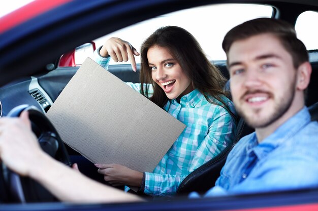 Lindo casal jovem sentado no carro e olhando para a câmera, sorrindo, feliz, apontando no mock up, espaço de cópia, mock up.